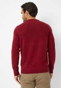 Maglione rosso lavorato a maglia con un design a costine testurizzate sulla parte superiore della schiena e sulle maniche, caratterizzato da un corpo liscio e un orlo lavorato a maglia.