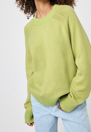 Pull en maille vert clair avec un col arrondi, des poignets et un bas côtelés, et une coupe décontractée. Associé à un jean bleu clair.