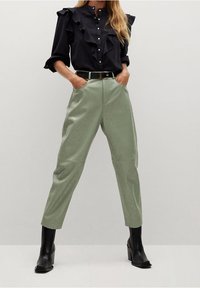 Blusa negra con volantes y botones, combinada con pantalones tapered de cintura alta en verde claro. Terminada con botas de tacón negras.