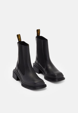 Czarne skórzane buty Chelsea z grubymi, kwadratowymi obcasami, elastycznymi panelami po bokach oraz żółtymi, z logo, pętelkami z tyłu.