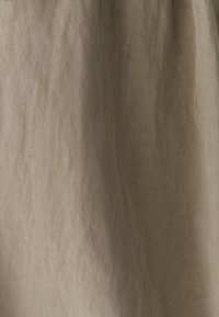 Tessuto beige con un motivo di intreccio diagonale e sottili pieghe verticali, illuminato da una luce soffusa.