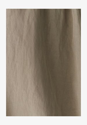 Bežs audums ar diagonālu austuma rakstu un maigiem vertikāliem krokām, izgaismots ar maigu apgaismojumu.