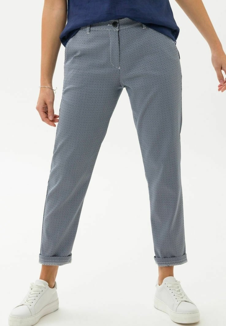 Personne portant un pantalon gris à motifs slim-fit retroussé, avec bouton et fermeture éclair devant, associé à des baskets blanches à plateforme.