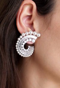 Silver earrings with a curved design, featuring pearls and rhinestones. The texture includes smooth and faceted surfaces with a glossy finish.