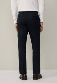 Donkere visgraatbroeken met een getailleerde pasvorm, voorzien van twee achterzakken en gepolijste schoenen, gestyled met een wit overhemd met lange mouwen.