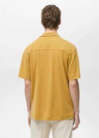 Short-sleeve, collared shirt in mustard yellow fabric. Features a relaxed fit with a smooth texture and a back yoke detailing.