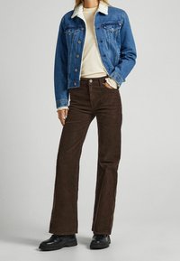 Blauwe jeansjack met een witte schapenvacht kraag, gecombineerd met donkerbruine corduroy broek. Zwarte veterschoenen maken de outfit compleet.
