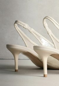 Smėlio spalvos aukštakulniai sandalai su plonais dirželiais, blizgiu paviršiumi ir tekstūruota vidpadžio dalimi. Pagaminti su plona stiletto tipo pakulne, kurios akcentas kontrastuoja.