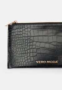 Denarnica s črnimi krokodiljimi vzorci, izdelana iz umetnega usnja, z zlatim zadrgo in logotipom "VERO MODA" v zlati barvi na dnu.