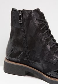 Bottine en daim et cuir noir avec fermeture éclair latérale, lacets noirs et petit talon empilé, présentée en gros plan.