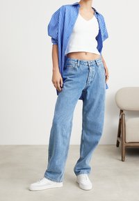 Vaaleansiniset denim-farkut, joissa on rento muotoilu, yhdistettynä valkoiseen lyhytvartiseen toppiin ja sinivalkoraidalliseen ylimääräiseen paitaan. Valkoiset tennarit.