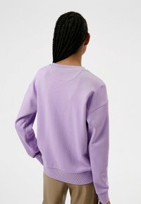 Sudadera de lavanda con un corte relajado, cuello redondo y dobladillo acanalado. La tela tiene una textura suave, con costuras de hombro caídas para mayor comodidad.
