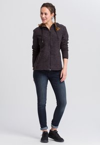 Mørk grå hættetrøje med lynlås og et tekstureret mønster, der har en hætte, to frontlommer, båret over mørke slim fit jeans og sorte sneakers.