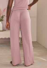 Pantaloni a gamba larga a coste di colore rosa chiaro con una texture morbida, dotati di una cintura smock e orli sfilacciati, visti da dietro.