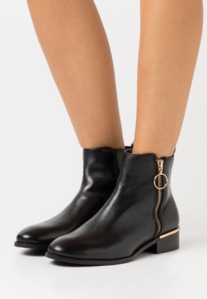 Černé kotníkové kozačky z kůže se zaoblenou špičkou, bočním zipem a zlatým detailem na nízkém block podpatku. Hladká textury, elegantní design.