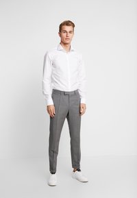 Witte overhemden met knopen, gecombineerd met lichtgrijze, op maat gemaakte broeken en witte sneakers. Glad materiaal met een aansluitend ontwerp en subtiele kreukdetails.