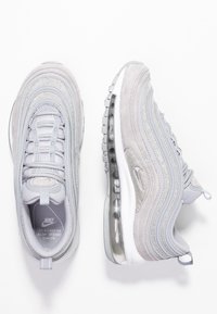 Grå Nike Air Max 97 sneakers i en blandning av mesh och mocka, med metalliska silverdetaljer, framträdande luftdämpning och texturerade ytor.