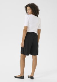 Pantaloni corti neri con vita elastica realizzati in un tessuto morbido, abbinati a una maglietta bianca aderente, visti da dietro. Design semplice con dettagli minimi.