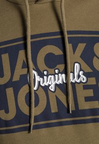 Sudadera verde oliva con acentos en azul marino; presenta grandes letras amarillas "JACK & JONES" y la palabra "Originals" en cursiva blanca. Incluye cordones con puntas metálicas.