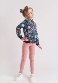 Kurtka z zamkiem błyskawicznym w kwiatowy wzór w granatowym kolorze, zdobiona żywymi różowymi, pomarańczowymi i zielonymi kwiatami; w zestawie z miękkimi różowymi legginsami i białymi sneakersami.