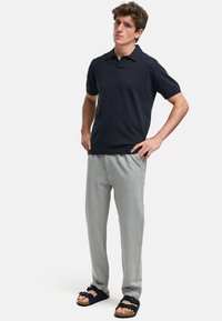 Polo skjorte i marineblå, laget av teksturert stoff, kombinert med lysegrå joggebukser og svarte sandaler med justerbare stropper.