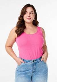 Enganliegendes pinkes Tanktop aus weichem Material mit rundem Ausschnitt, kombiniert mit hoch sitzenden hellblauen Jeans.