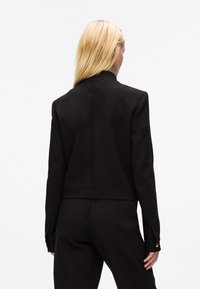 Giacca nera su misura con un design strutturato, colletto a revers e polsini con bottoni. Tessuto liscio e lunghezza cropped.