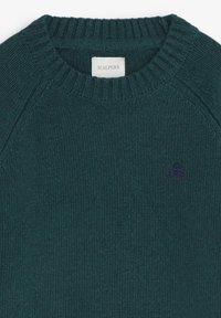 Suéter de punto verde oscuro con cuello redondo acanalado y mangas raglán. Presenta un pequeño logo morado de una calavera con huesos cruzados.