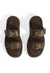 Sandales en cuir marron avec deux sangles réglables à boucle, une semelle intérieure rembourrée et une semelle extérieure noire contrastante. Texture lisse et design minimaliste.