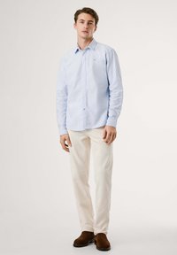 Lys blå skjorte med lange ermer, kombinert med kremfargede bukser og brune sko. Stoffet ser glatt ut med en subtil tekstur.