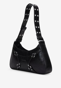 Bolso de mano de cuero negro con forma curvada, que presenta una correa con tachuelas y detalles en material plateado. Textura lisa con un brillo sutil.