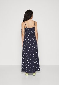 Robe longue bleu marine à pois blancs, avec des bretelles spaghetti réglables et une taille cintrée. Le tissu tombe doucement jusqu'au sol.
