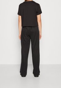 Černé zkrácené tričko s krátkým rukávem, kombinované s volnými černými tepláky s bílými bočními pruhy. Hladký textilní materiál.