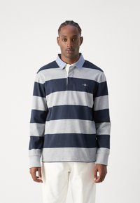 Hosszú ujjú galléros póló tengerészkék és szürke vízszintes csíkokkal, klasszikus gallérral, sliccelt gombsorral és hímzett logóval a mellrészen.