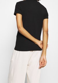 Sort kortærmet t-shirt lavet af bomuld, med rund hals og en tætsiddende pasform. Sammen med lette, teksturerede, brede bukser.