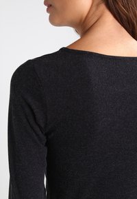 Schwarzes Langarmshirt aus einem weichen, strukturierten Stoff, mit einem weitem Ausschnitt und enganliegenden Ärmeln.
