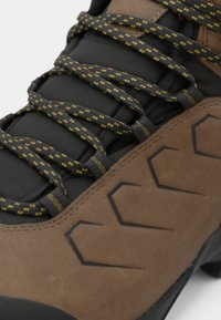 Bota de senderismo marrón con parte superior de ante texturizado, acentos negros y cordones gris y amarillo con patrón. Presenta una suela de goma con diseño geométrico que ofrece agarre.