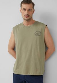T-shirt sans manches vert olive en coton, avec un logo circulaire en impression foncée sur la poitrine. Coupe décontractée avec un col ras du cou.