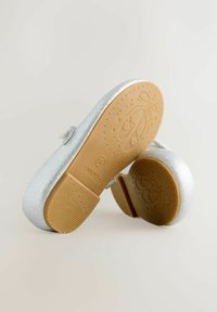 Glittery silver ballet shoes with a round toe, adjustable strap, and a beige rubber sole featuring a ballet shoes pattern and textured grip.