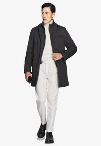 Mørkegrå uldfrakke med et struktureret design, båret over en cremet turtleneck, parret med hvide bukser og sorte ankelstøvler.