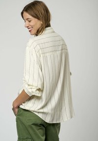 Chemise blanche à manches longues avec de fines rayures vertes, manches retroussées et coupe décontractée. Comprend un dos plissé et un tissu doux et texturé.
