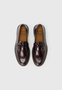 Σκούρα βουργουνδίας δερμάτινα παπούτσια με στρογγυλεμένη μύτη και διακοσμητικό λουράκι με αγκράφα. Ομαλή υφή με αντίθετη μαύρη σόλα.