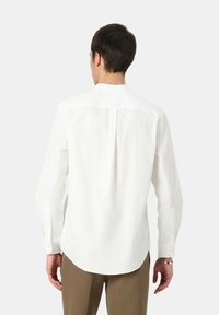 Camicia bianca a maniche lunghe con taglio dritto, polsini con bottoni, dettagli con piega sul retro e tessuto morbido e strutturato. Adatta per abbigliamento casual o formale.