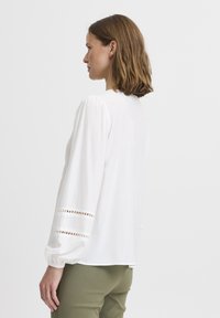 Weiße Bluse mit puffärmel, die über ausgeschnittene Details an den Manschetten verfügt. Weicher, leichter Stoff mit lockerer Passform und runder Halslinie.
