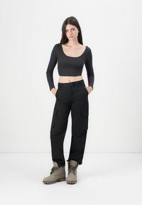 Un top negru, cu mâneci lungi și croială scurtă, asociat cu pantaloni cargo negri, cu talie înaltă, având buzunare laterale și botine bej. Material neted și ajustat.