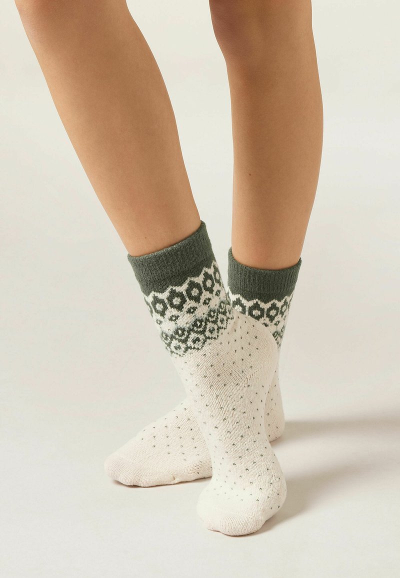 Strikkede sokker i creme med en grøn mønstret kant, der har et blomstermotiv og teksturerede prikker over hele kroppen.