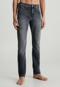 Mörkgrå denimjeans för män med slim fit. Har fem fickor, bälteshällor och en subtil gradientfade. Mjuk textur, medelvikt.
