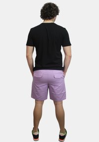 Camicetta nera a maniche corte, pantaloni corti lavanda con due tasche posteriori e scarpe da ginnastica nere con dettagli neon, viste da dietro.