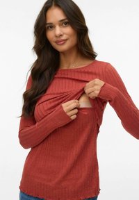 Ribbad långärmad topp i rostfärg, med rundad halsringning och en sidoförslutning som avslöjar ett sömlöst underlager. Texturerat tyg med rå fåll.