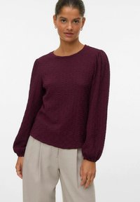 Bordeaux gekleurde blouse met textuur, lange mouwen, een ronde hals en gathered manchetten, gecombineerd met lichtgrijze op maat gemaakte broek.